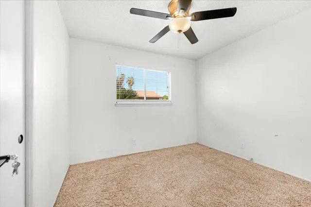 an empty room with a chandelier fan and windows
