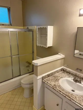 a bathroom with a granite countertop sink a toilet a mirror and shower