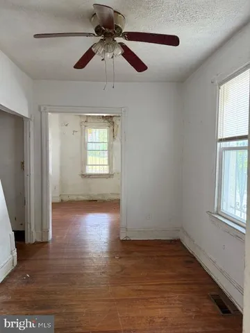 an empty room with wooden floor chandelier fan and windows