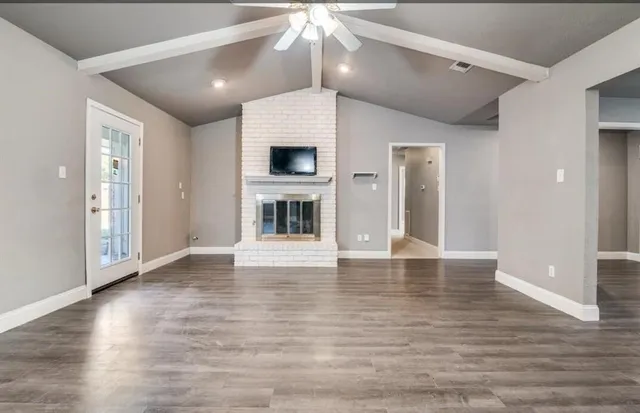 a view of an empty room with wooden floor fireplace and a window