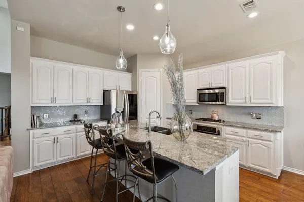 a kitchen with stainless steel appliances kitchen island granite countertop a sink dishwasher a stove a refrigerator a microwave oven with white cabinets and wooden floor