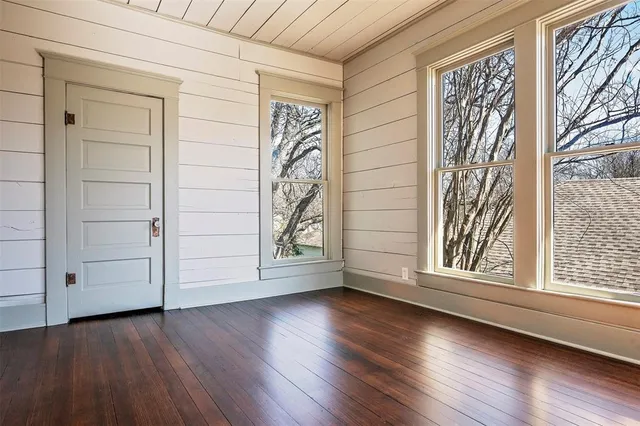 an empty room with wooden floor and windows with curtains