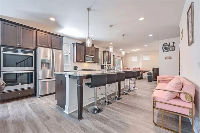 a kitchen with stainless steel appliances kitchen island granite countertop a refrigerator a oven a stove top oven and a dining table with wooden floor