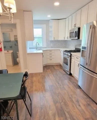 a kitchen with a refrigerator a stove top oven a sink dishwasher and white cabinets with wooden floor