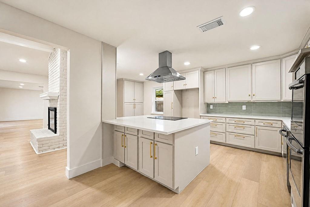1904 Apollo Road Richardson, TX 75081 - Photo 13 of 40 Modern kitchen with a large island, stainless steel range hood, light wood-finish flooring, and light-toned cabinetry with gold-tone hardware