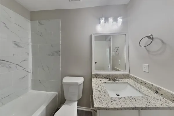 a bathroom with a granite countertop sink a toilet and bathtub