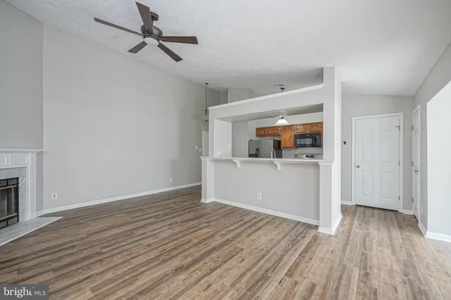 a view of a room with wooden floor a kitchen space and a ceiling fan