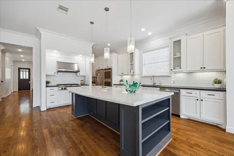 a kitchen with stainless steel appliances kitchen island granite countertop a stove a sink and white cabinets with wooden floor