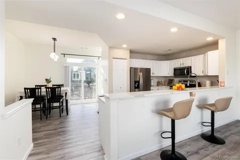 a kitchen with stainless steel appliances granite countertop a refrigerator a stove a sink a dining table and chairs with wooden floor