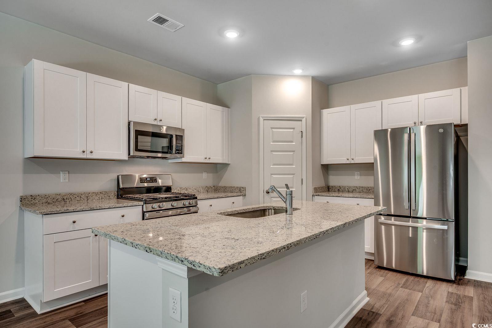 1004 Sentinel Court Little River, SC 29566 - Photo 4 of 31 Kitchen featuring light stone counters, appliances with stainless steel finishes, white cabinetry, dark wood-style floors, and an island with sink