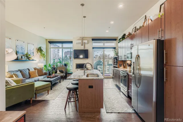 a living room with stainless steel appliances furniture a rug and a kitchen view