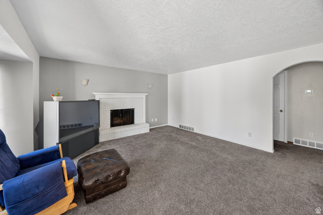 1218 East 100 South Logan, UT 84321 - Photo 10 of 23 Spacious living area featuring neutral carpeting, a white brick fireplace, and an arched doorway