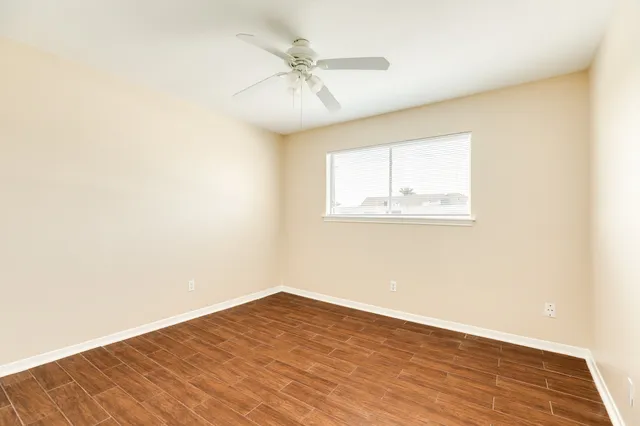 an empty room with wooden floor fan and windows