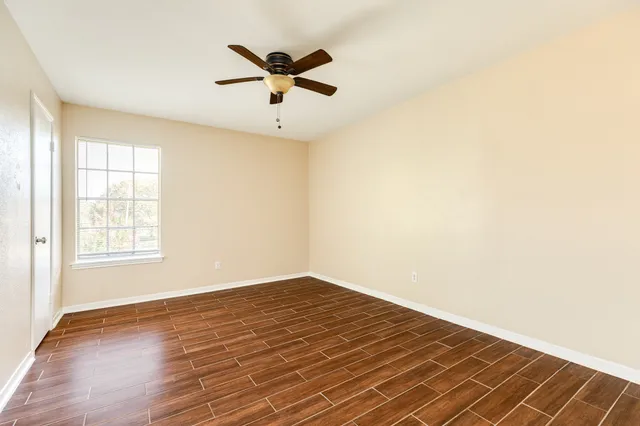 an empty room with wooden floor fan and windows