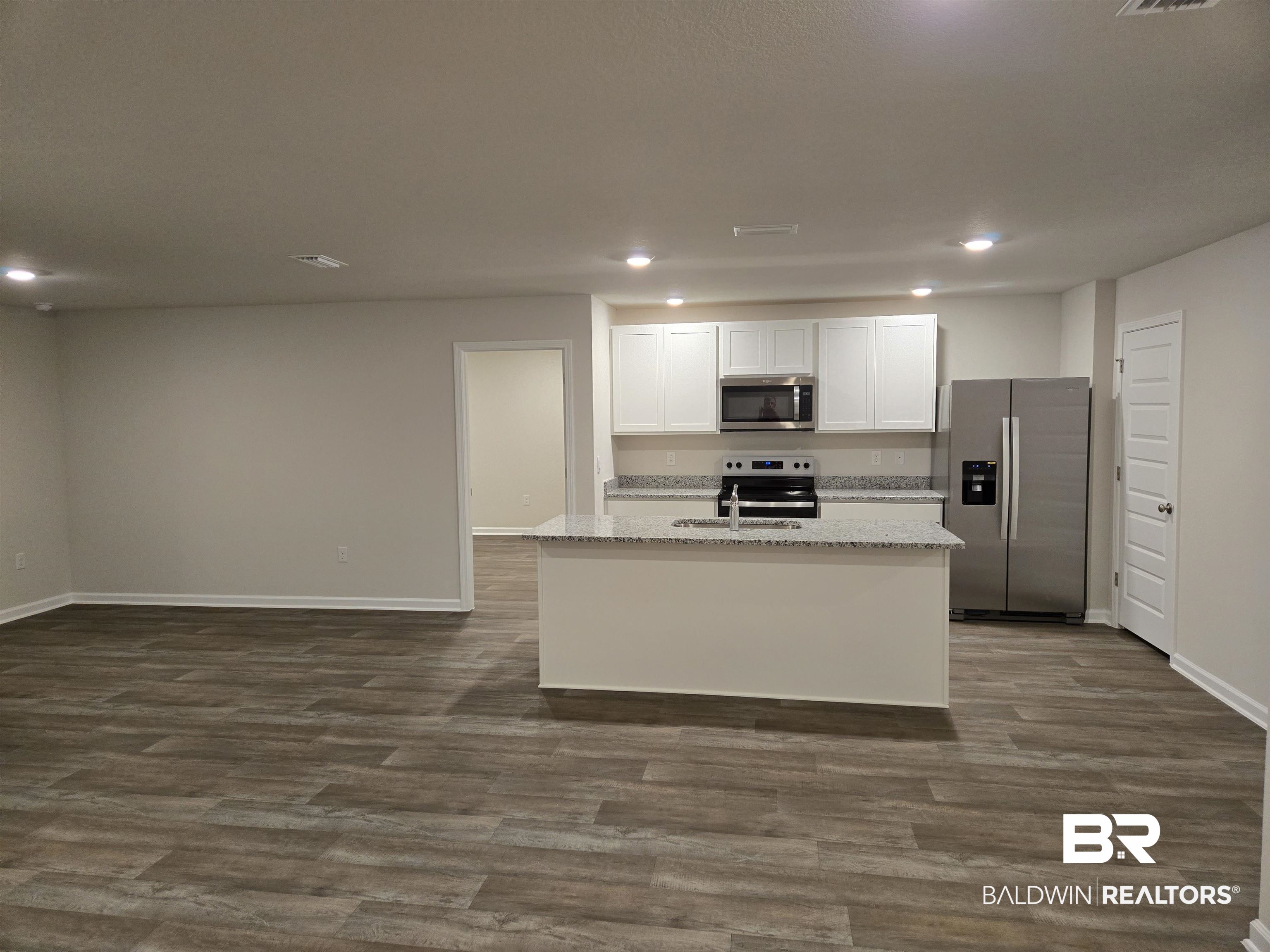 24194 Veranda Circle Elberta, AL 36530 - Photo 19 of 31 Kitchen with light stone counters, stainless steel appliances, a kitchen island with sink, dark wood-type flooring, and white cabinetry