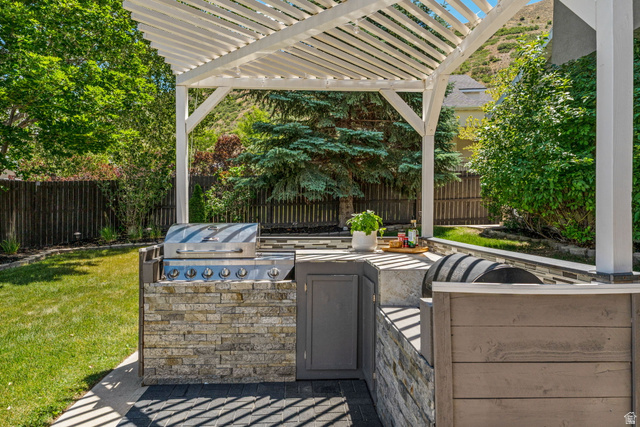14883 Tooele Lane Draper, UT 84020 - Photo 7 of 49 Outdoor kitchen featuring a built-in stainless steel grill, stone veneer base, and a white wood pergola