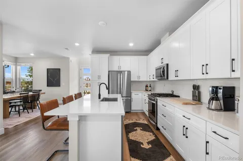 a kitchen with stainless steel appliances granite countertop a refrigerator a stove a sink a dining table and chairs with wooden floor