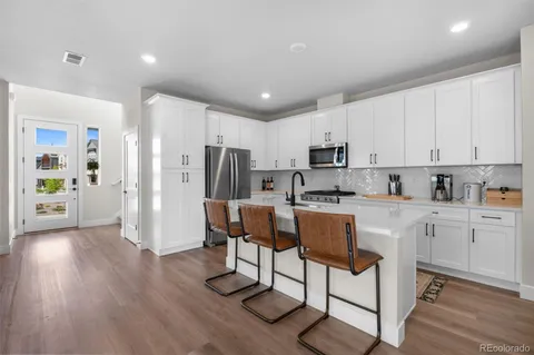 a kitchen with stainless steel appliances granite countertop a refrigerator a stove top oven a sink dishwasher and white cabinets with wooden floor