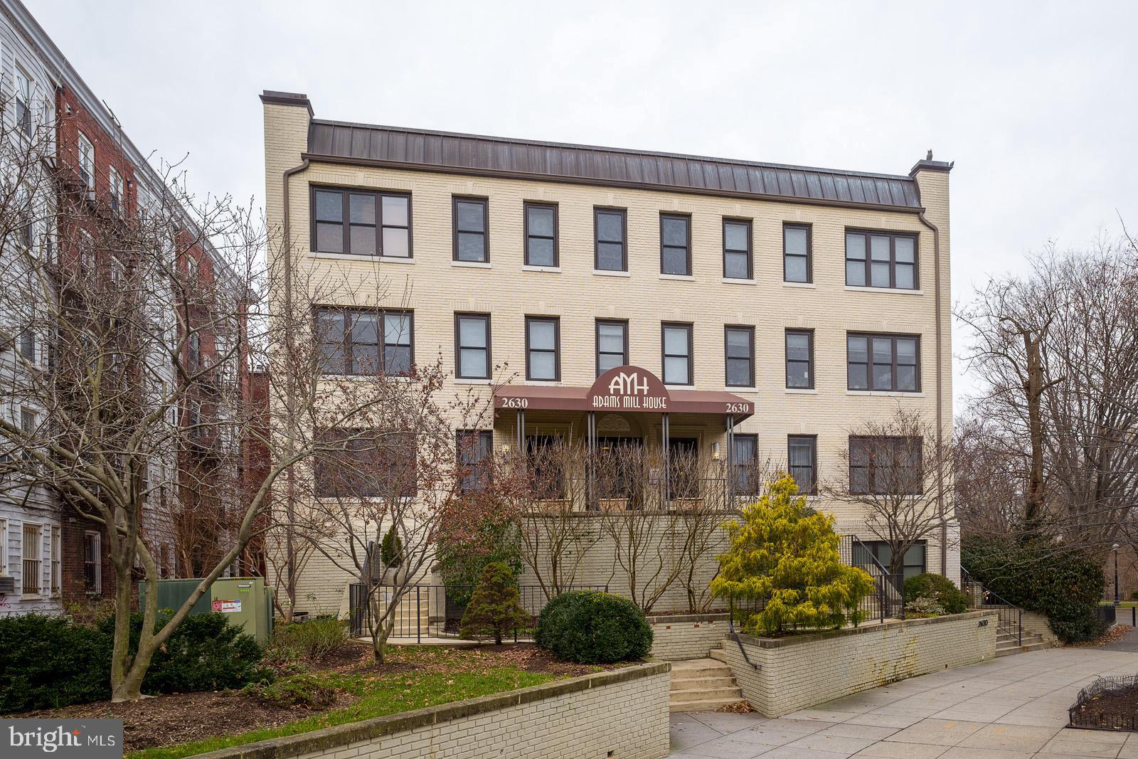 a front view of a building with garden and trees