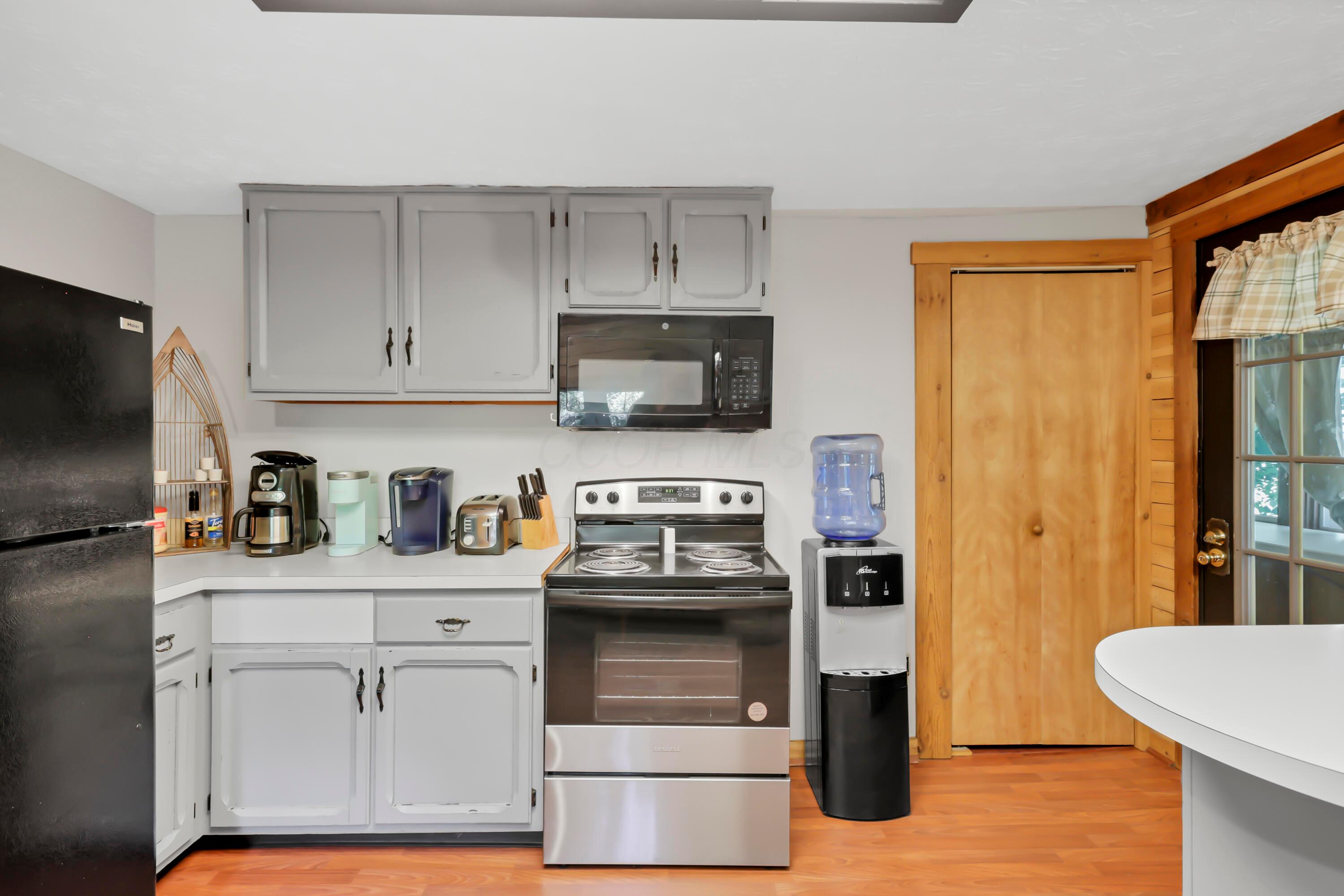 9126 Walnut Dowler Road Logan, OH 43138 - Photo 14 of 41 Updated kitchen featuring white cabinetry with hardware accents, stainless steel appliances including a slide-in electric range and microwave, laminate countertops, and wood-finish flooring