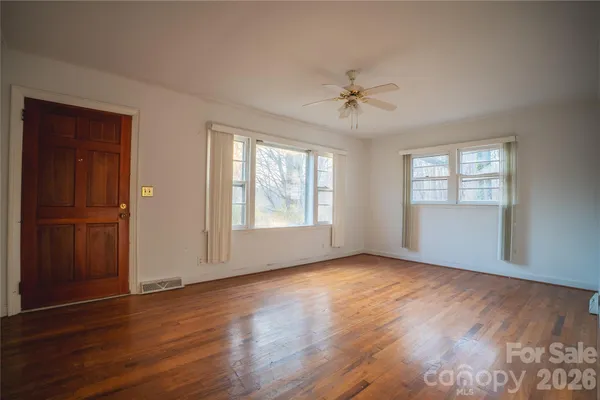 an empty room with wooden floor chandelier fan and windows