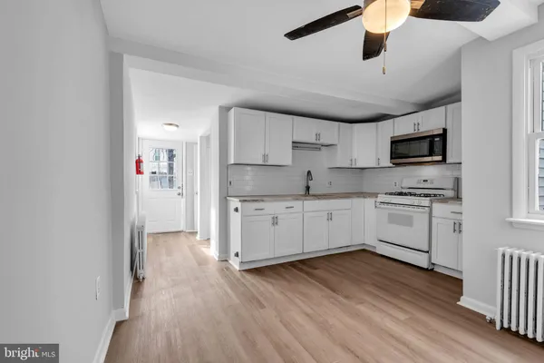 a kitchen with granite countertop a refrigerator a sink dishwasher a stove and white cabinets with wooden floor