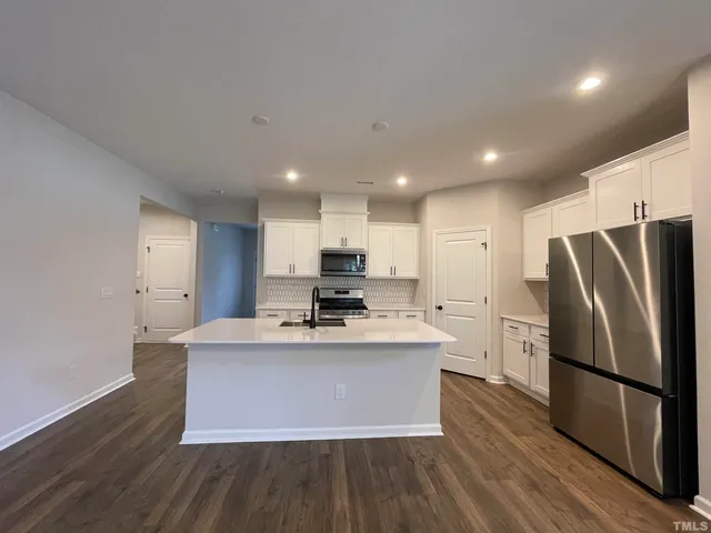 a kitchen with kitchen island a sink a stove a refrigerator and white cabinets with wooden floor