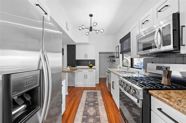 a kitchen with stainless steel appliances granite countertop a stove top oven a sink dishwasher a refrigerator and cabinets with wooden floor