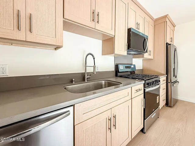 a kitchen with stainless steel appliances granite countertop a sink a stove and a refrigerator with wooden floor