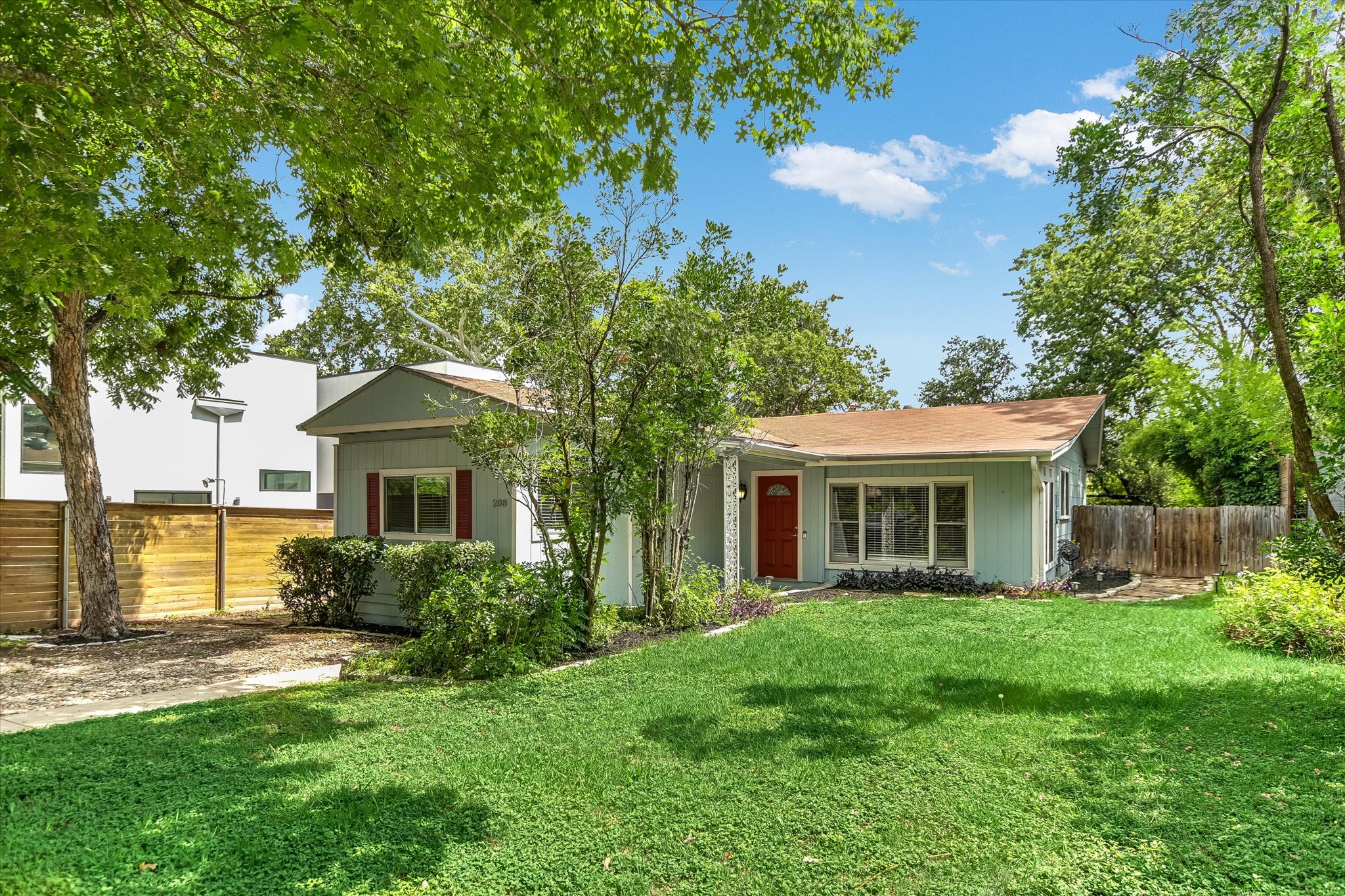 208 Braeswood Road Austin, TX 78704 - Photo 2 of 20 A well-maintained lawn and mature trees frame this inviting residence, featuring a vibrant red entry door.