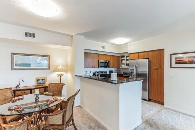 a kitchen with stainless steel appliances kitchen island granite countertop a dining table chairs and a refrigerator