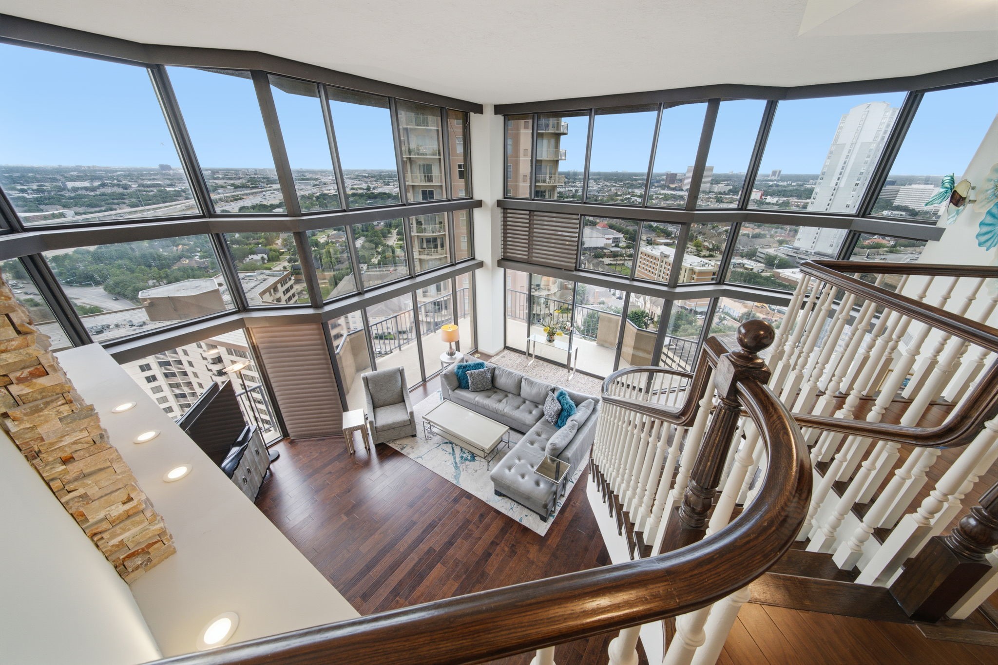 3350 McCue Road, Unit 2402 Houston, TX 77056 - Photo 28 of 49 Viewed from the upper mezzanine, the grand living salon reveals an impressive two-story glass enclosure showcasing sweeping urban vistas. Gleaming hardwood floors, an elegant curved staircase banister, and stacked-stone architectural accents enhance the dramatic scale of elevated high-rise entertaining.