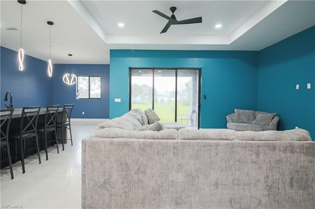 3902 4th Street Southwest Lehigh Acres, FL 33976 - Photo 13 of 34 Tray ceiling with a black ceiling fan, modern pendant lighting, sliding glass door, and a kitchen island with a dark countertop