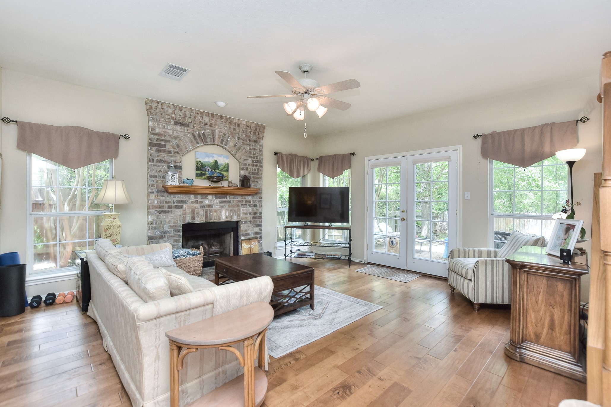 1609 Colton Way Cedar Park, TX 78613 - Photo 6 of 24 A welcoming living area showcases a substantial brick fireplace, hardwood floors, and French doors opening to outdoor green space.