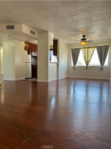 a view of empty room with wooden floor and kitchen