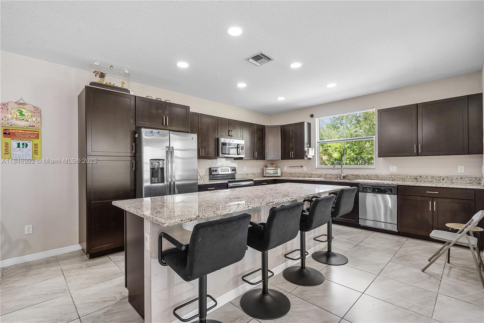 6411 Osprey Landing Street Davie, FL 33314 - Photo 12 of 38 a kitchen with stainless steel appliances granite countertop a table chairs sink refrigerator and microwave