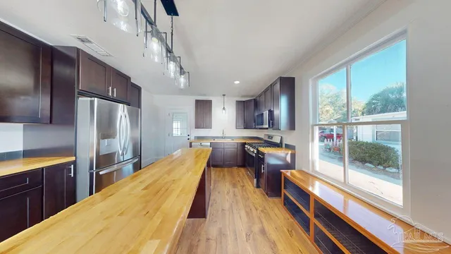 a view of a kitchen with kitchen island wooden floors stainless steel appliances and windows