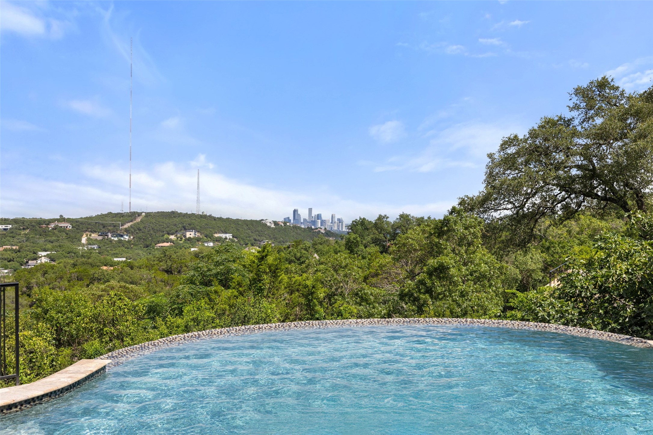 1414 The High Road Austin, TX 78746 - Photo 5 of 40 A tranquil infinity pool overlooking a verdant hillside and distant city skyline.