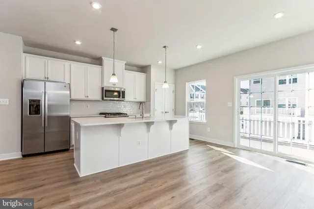 a kitchen with stainless steel appliances granite countertop a refrigerator a sink dishwasher a stove and white cabinets with wooden floor