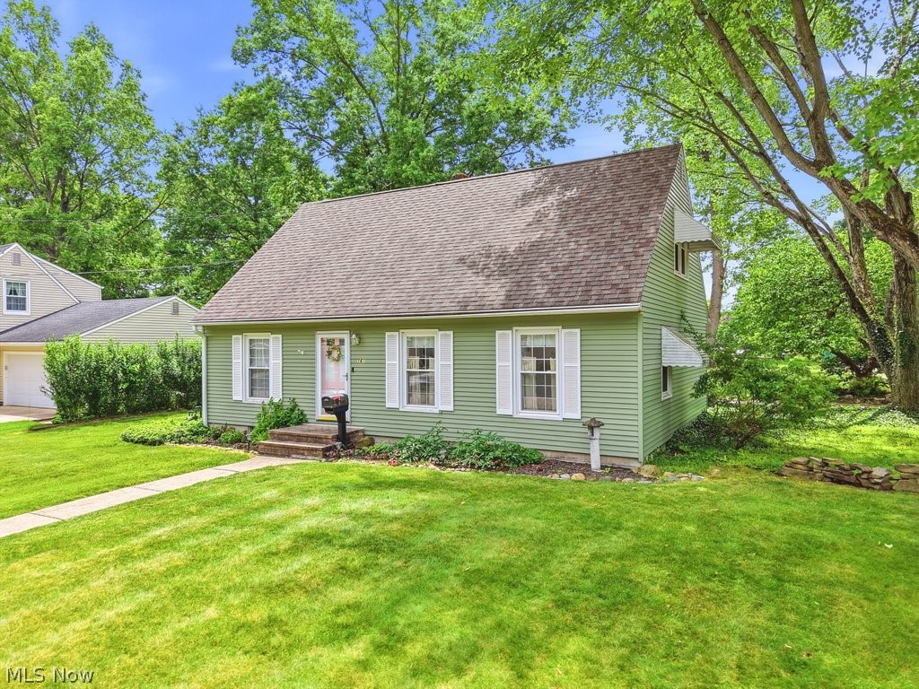 161 Pinehurst Road Munroe Falls, OH 44262 - Photo 3 of 40 Light green siding home with white window shutters and awnings, featuring a front lawn, mature trees, and a stone walkway