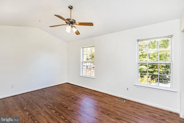 an empty room with wooden floor fan and windows