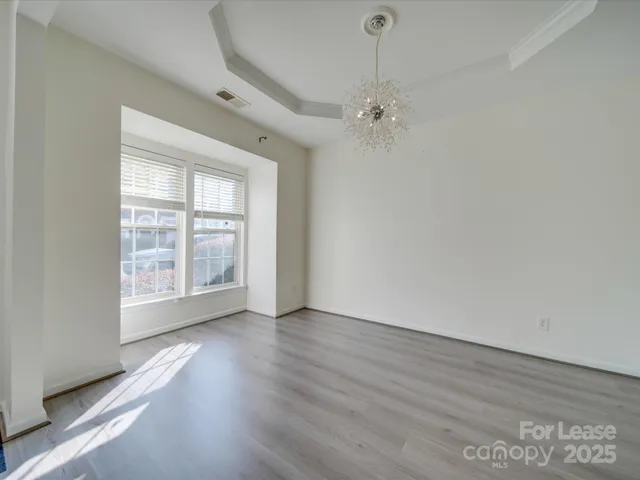 an empty room with wooden floor chandelier fan and windows
