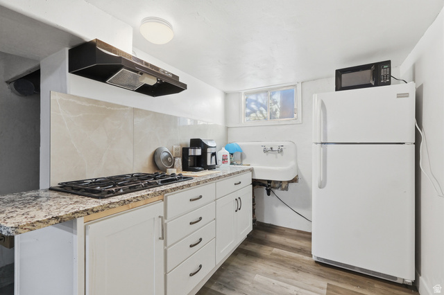 202 Main Street Smithfield, UT 84335 - Photo 24 of 32 Kitchen featuring black appliances, light wood finished floors, ventilation hood, white cabinetry, and tasteful backsplash