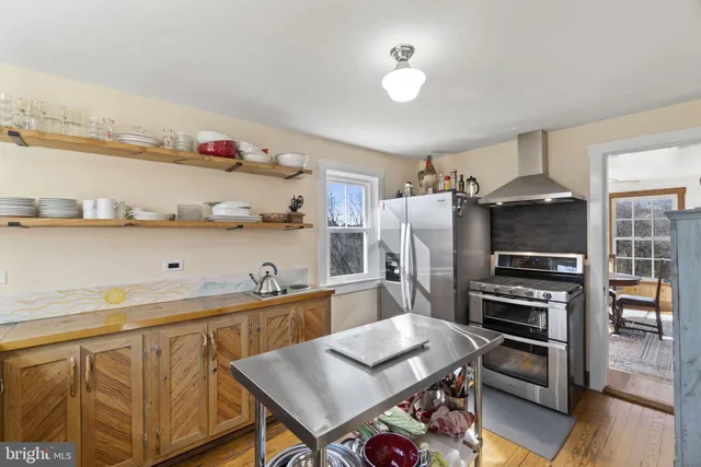 a kitchen with stainless steel appliances a stove a refrigerator and a dining table with wooden floor