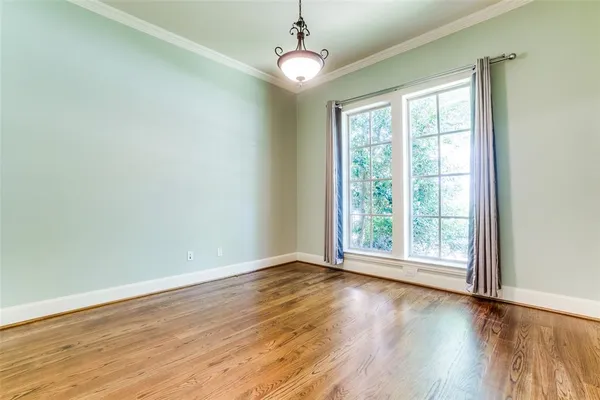 a view of an empty room with wooden floor chandeliers and a window
