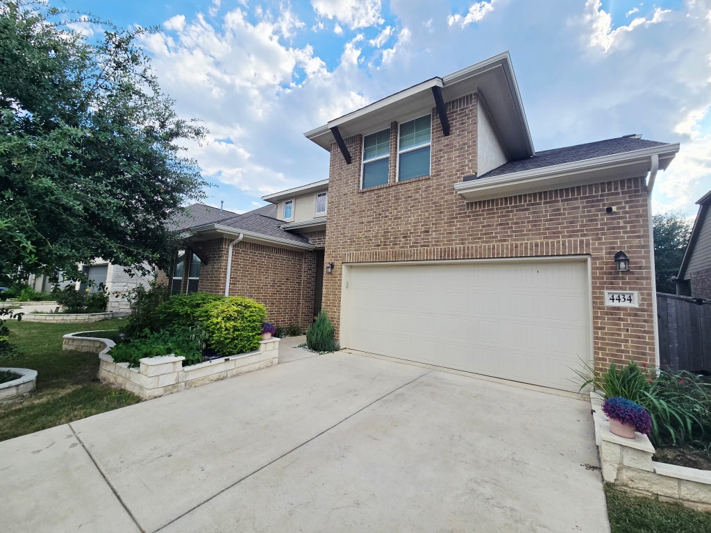 Traditional-style house featuring brick siding, driveway, and an attached garage