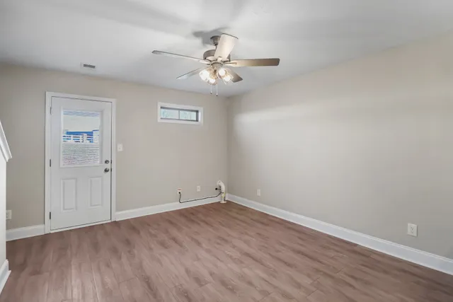 an empty room with wooden floor fan and windows
