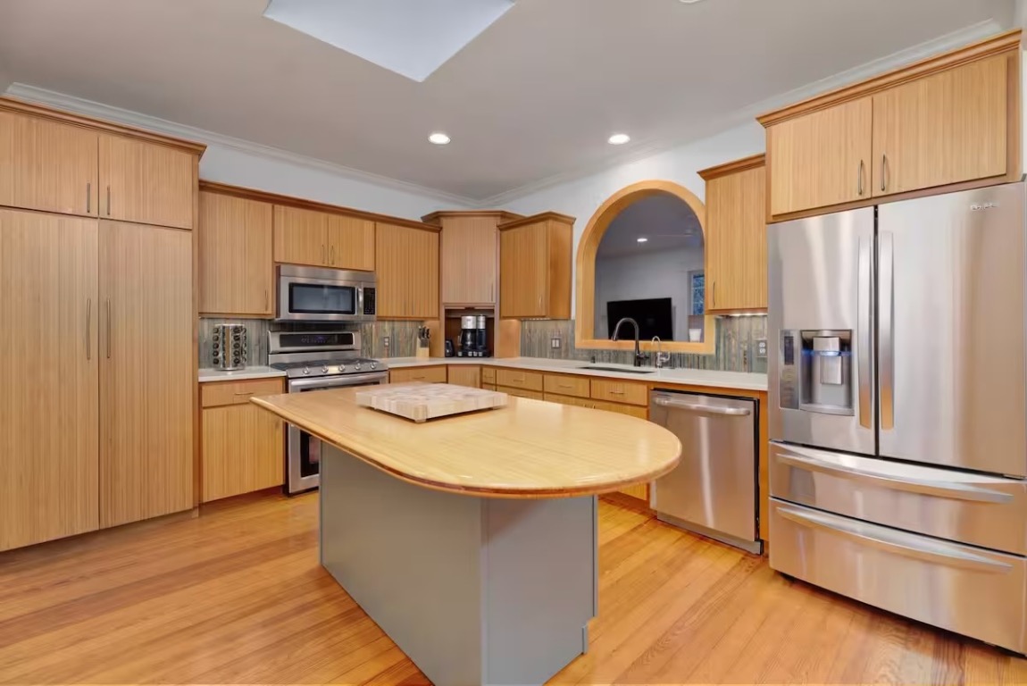 1212 Baylor Street Austin, TX 78703 - Photo 3 of 14 Kitchen featuring appliances with stainless steel finishes, light wood-style floors, a center island, decorative backsplash, and crown molding