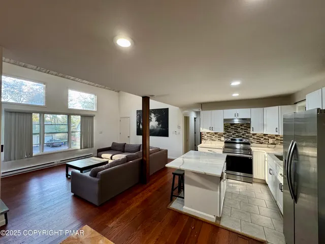 a living room with stainless steel appliances kitchen island granite countertop a refrigerator a stove a sink dishwasher with a dining table and chairs with wooden floor
