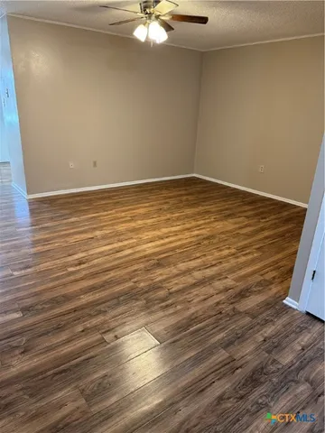 a view of an empty room with wooden floor and fan